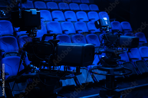 Professional broadcast cameras recording in an empty television studio, preparing for a media production or live news event with rows of blue audience seats
