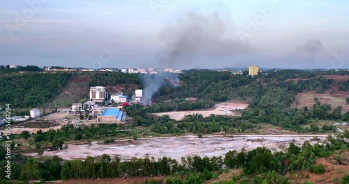 Aerial view of smoke and fire in a forested area near urban buildings.