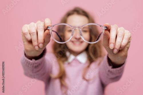 Tableau sur toile Clear eyeglasses held in hands with smiling woman blurred on pink background