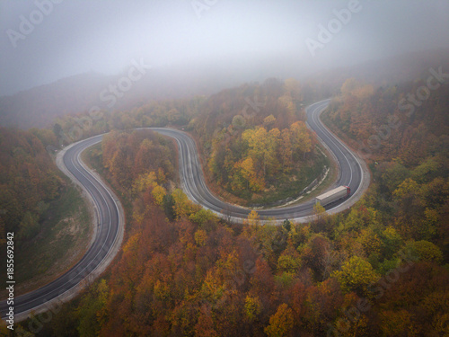 Aerial view of a single car driving on a winding foggy mountain road at sunrise