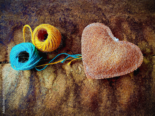 Two rolls of yarn and Luffa heart shape,texture is coarse and fibrous.put on vintage wooden board,blurry light around