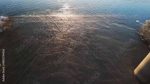 Wide Aerial Over Reflective Wet Sand Underneath Pier With Soft Sunlight Glint Expansive Composition Shows Wet Beach, Gentle Surf, Pier Supports At Edges And Calm Horizon For Lifestyle, Travel