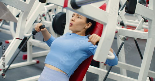 Gym workout. Bench press in hammer machine. A Caucasian woman trains her chest muscles with focused bench press reps on the hammer machine during an intense gym workout.