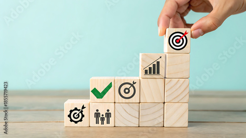 Hand Placing Target Icon Block on Staircase of Wooden Blocks with Business Icons, Achieving Goals