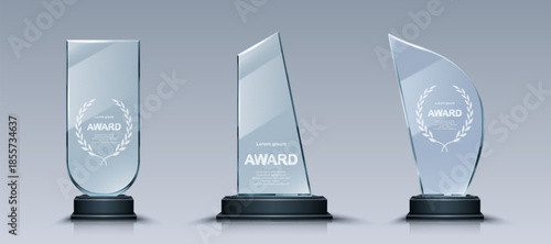 Glass trophy set with elegant laurel wreath engravings on crystal plates. Transparent award collection with unique glass shapes on dark pedestals designs for business or sport recognition ceremonies.