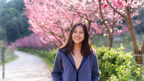 A young woman is standing amidst the cherry blossom trees.