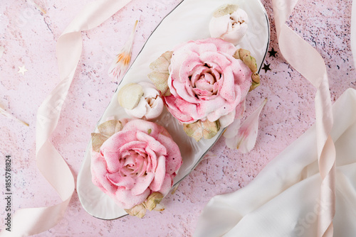 Soft pastel flat lay with handcrafted berry zephyr and marshmallow shaped like flowers, tea set and flowing fabric.