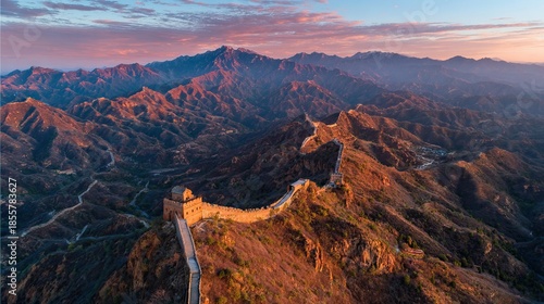 Aerial view of the Great Wall of China at sunrise with mountains in the background.
