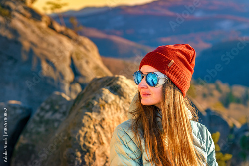 Active woman in red beanie hiking rocky mountains at golden hour, warm outdoor clothing