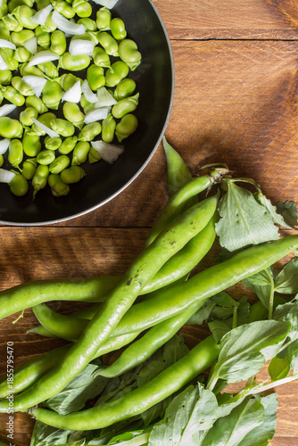 Closed broad bean pods with shelled broad beans in a pan
