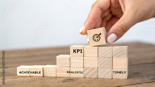 Hand places KPI block onto stair-step stack of wooden blocks with business strategy words