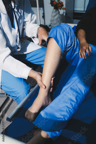 Asian male doctor examining foot of female patient sitting on bed in hospital room. Performing medical checkup. Diagnosing injury. Providing healthcare. Podiatry. Physical therapy. And rehabilitation
