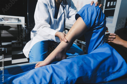 Asian male doctor examining foot of female patient sitting on bed in hospital room. Performing medical checkup. Diagnosing injury. Providing healthcare. Podiatry. Physical therapy. And rehabilitation