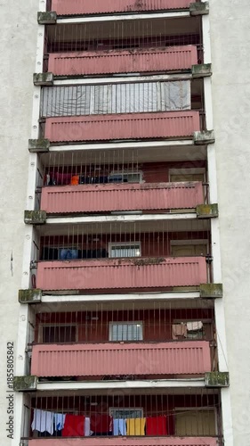 Stacked Balconies With Colorful Laundry Drying, Worn Concrete Facade With Metal Railings And Red Awnings, Hinting At Everyday Routines And Community Life In Compact Urban Apartment Block.