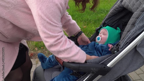 mother lifting baby from stroller on paved path in green park, capturing a tender moment of caregiving, connection, and outdoor family routine in natural light