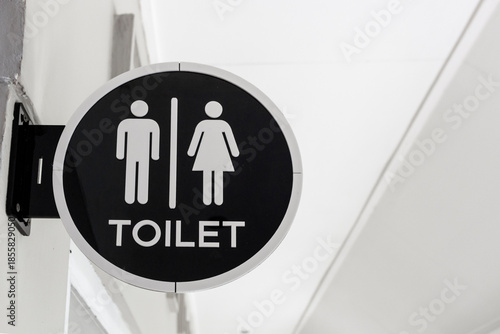 A modern, circular wall-mounted toilet sign featuring white male and female pictograms and the text 