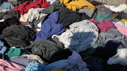 Pile of discarded and messy pile of various colorful used clothes outdoors in sunlight