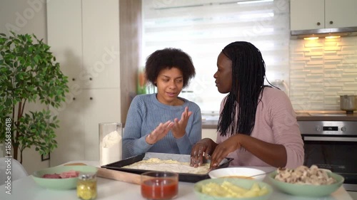 African american mother and daughter happily preparing pizza in the kitchen