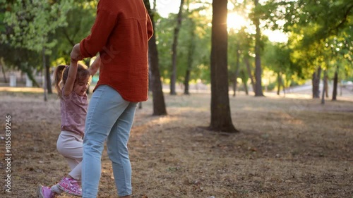 Mother spinning her happy daughter around in a park at sunset