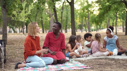 Multinational women caregivers talking during a picnic with children in the park