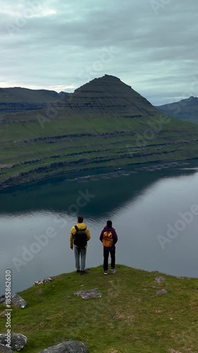 Hikers stand at the edge of a cliff, admiring the stunning landscape of Gonguturur Hvithamar Trail in the Faroe Islands.