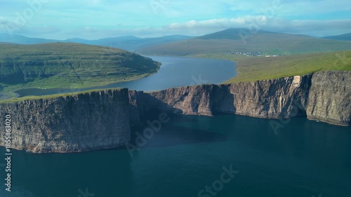 Stunning cliffs dominate the landscape around Lake Sorvagsvatn in the Faroe Islands. The tranquil water reflects the beauty of the surrounding hills and sky, creating a breathtaking view.
