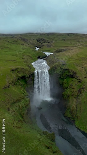 Majestic Skogafoss waterfall cascades down a rocky cliff, surrounded by vibrant green hills and a misty atmosphere. Ideal setting for nature lovers seeking stunning views and tranquility.