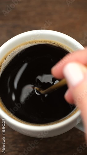 Add sugar to a cup of black coffee Female hand stirring sugar in mug of black coffee