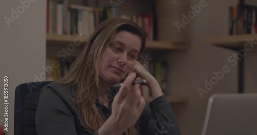 A woman in her office working at her laptop, procrastinating, and fidgeting with her pen, spinning it and dropping it.