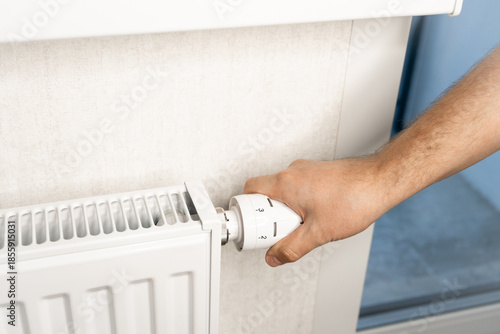 Photos Hand adjusting radiator valve for heating control in winter