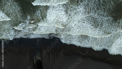 Aerial view of ocean waves crashing onto dark sandy beach