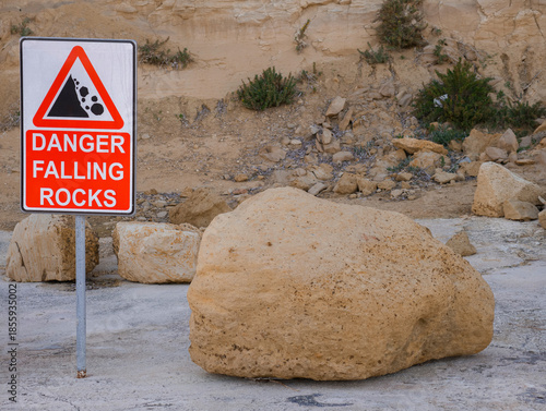 warning sign for falling rocks at coastal cliff with large boulder