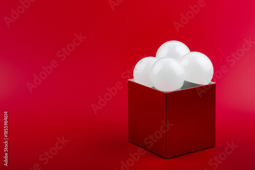 Four white LED bulbs standing vertically in a glossy cardboard box on bright red background. Creative thinking and innovation concept.