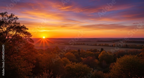 Radiant sun descends over rolling hills and dense forest canopy at dusk