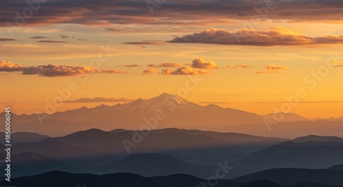 Distant snowcapped mountain peak rises above layered ridges during vibrant sunset