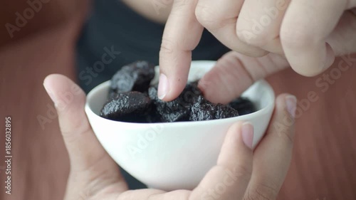 Close Up of Person Holding a White Bowl of Healthy Dried Prunes and Taking One to Eat