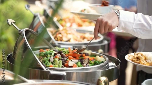 Close-up of Guest Serving Healthy Stir-Fried Vegetables from a Chafing Dish at an Outdoor Buffet Event