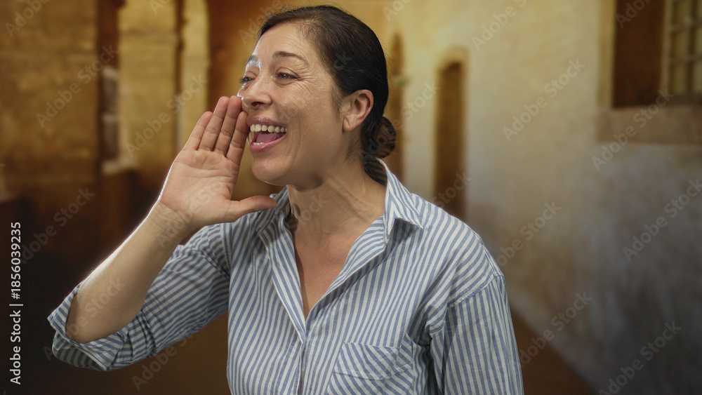 Fototapeta premium Woman calls with hand at mouth on historic old town street lined with stone buildings; social connection joy.