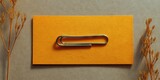 Minimalist Stationery: An elegant paper clip rests upon a vibrant yellow card, set against a backdrop of subdued tones, a study in simplicity and functionality. 