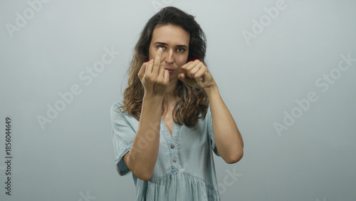 Fényképezés Woman wearing a denim dress raises a middle finger with direct gaze and clenches a fist in a grey studio; defiance