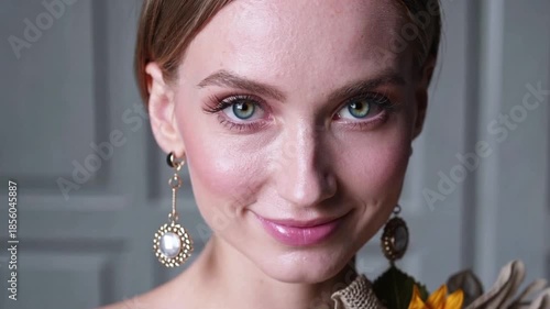 Elegant young woman with captivating blue eyes and elaborate vintage style drop earrings smiles softly showcasing her refined makeup and detailed accessories for a portrait session.