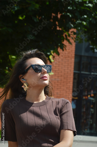 Stylish young Caucasian woman in sunglasses and brown dress on city street