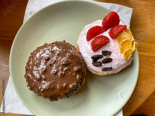 Two delicious donuts on a plate. One with chocolate glaze, the other with pink cream and strawberries.