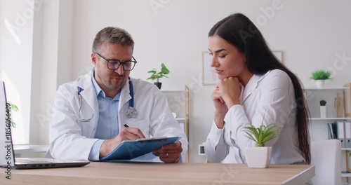 Young woman suffering from headache rubbing her temples during consultation in medical clinic. Physician or cardiologist listening to patient complaints, giving advices and describing treatment plan.
