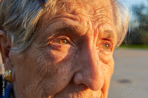 Close-up portrait of octogenarian woman with vivid green eyes and wrinkled skin bathed in warm autumn sunset light