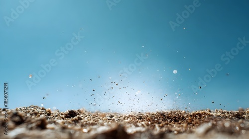 Close up of countless fine sand particles exploding upwards into a clear vibrant blue sky