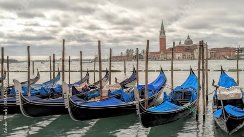 Gondolas docked in Venice, Italy, gently bobbing under a cloudy evening sky with a view of the skyline in the distance