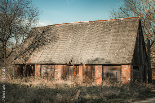 Old abandoned rural buildings. Decaying wooden door set in a cracked brick wall overgrown with plants. A symbol of passing time, neglect and forgotten places