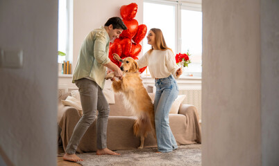 Joyful young couple playing and dancing with their dog at home, celebrating love, happiness and Valentine’s Day together.
