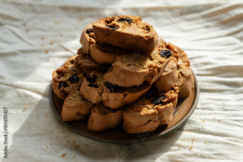 Stack of italian biscotti cantuccini cookies with nuts and raisins on a plate over white linen tablecloth